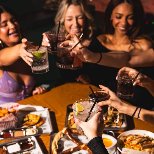 Group of friends toasting drinks over a table with shared appetizers and entrees