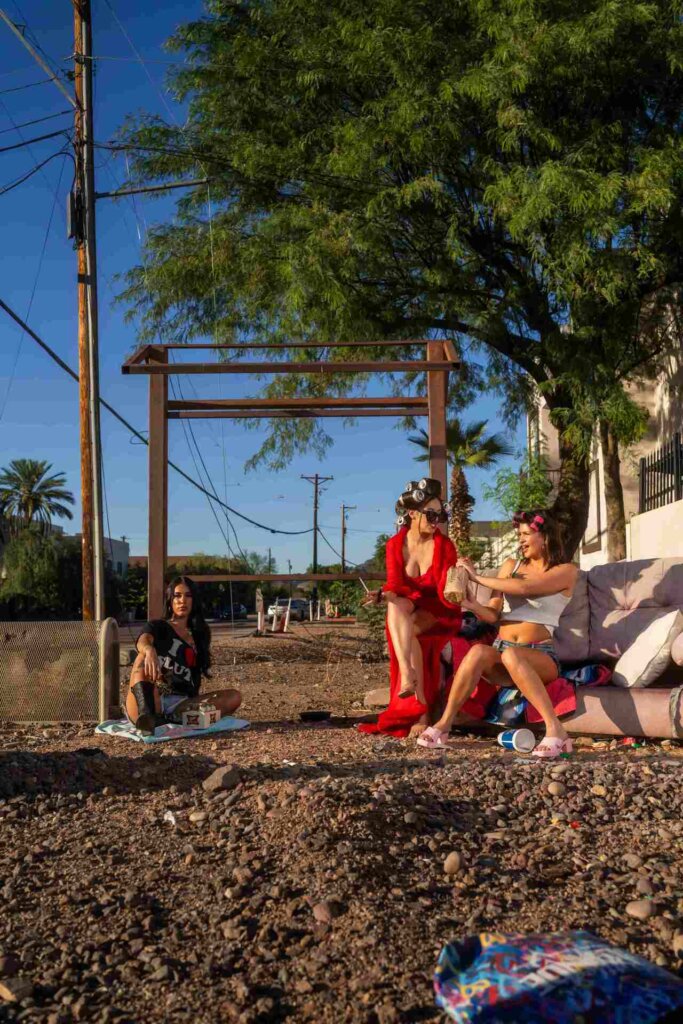 Friends hang out in a sunny trailer park setting, dressed in bright, vintage-inspired outfits. With drinks, laughter, and casual fun, this Mother Tucker’s Tavern moment captures carefree, small-town charm.