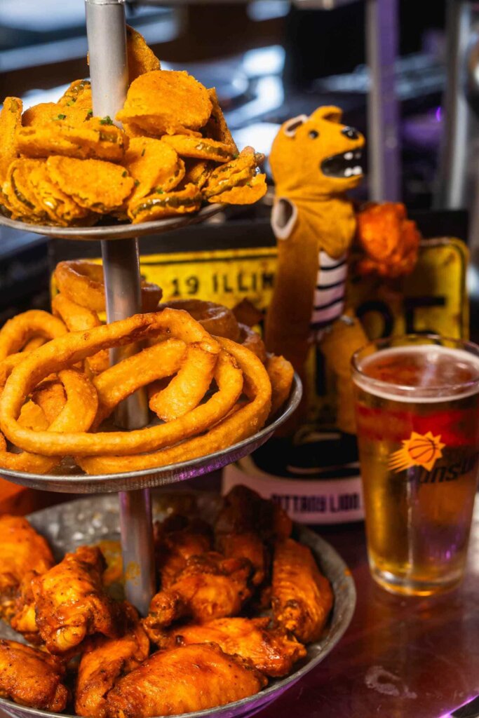 Mouthwatering fried appetizers including crispy onion rings, spicy buffalo wings, and fried pickles served on a metal tiered tray with a cold beer perfect for game day or bar snacks.