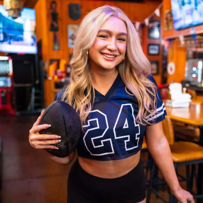 Woman wearing a football jersey holding a football inside a sports bar